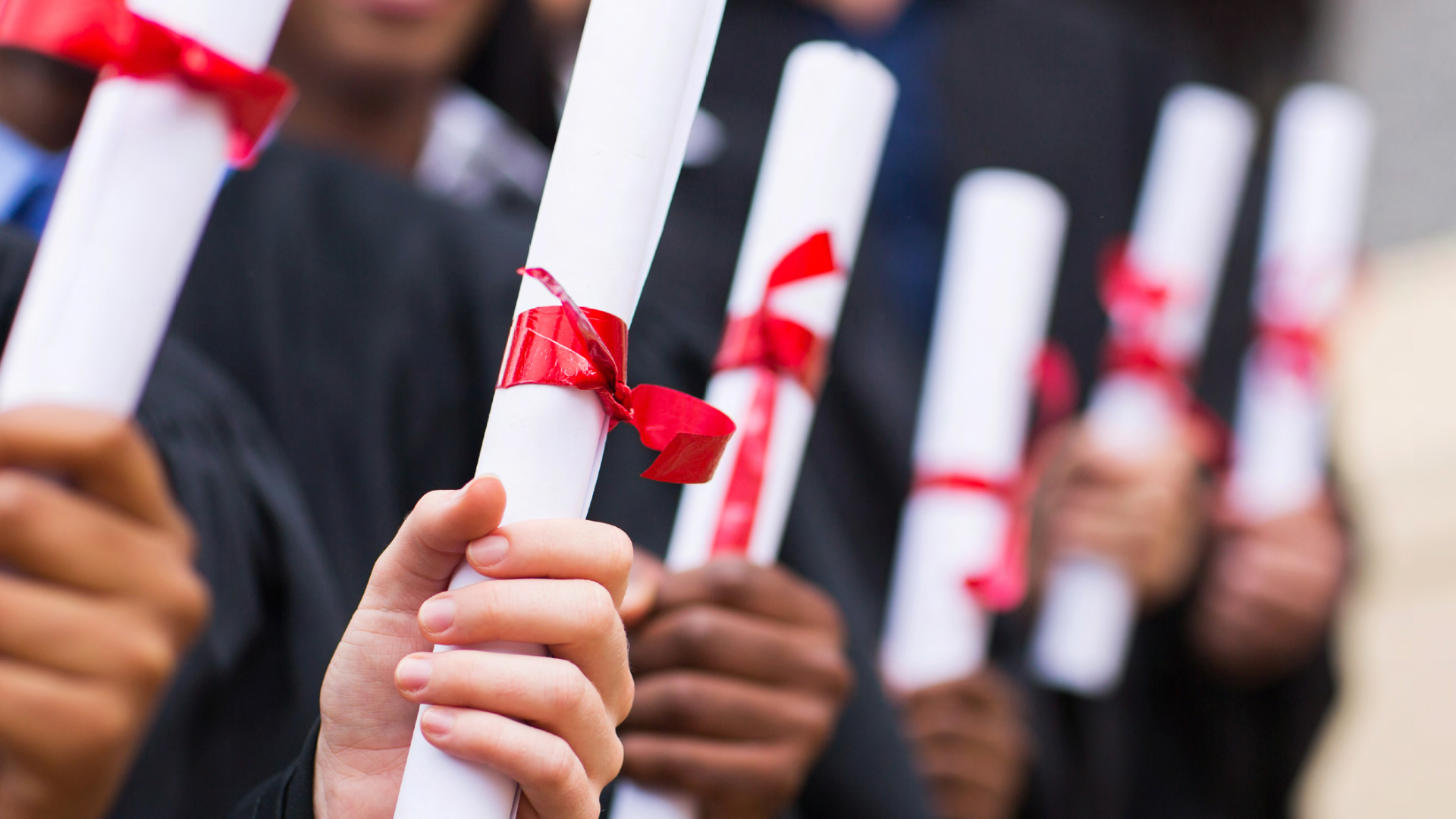 Students holding diplomas with red ribbons.